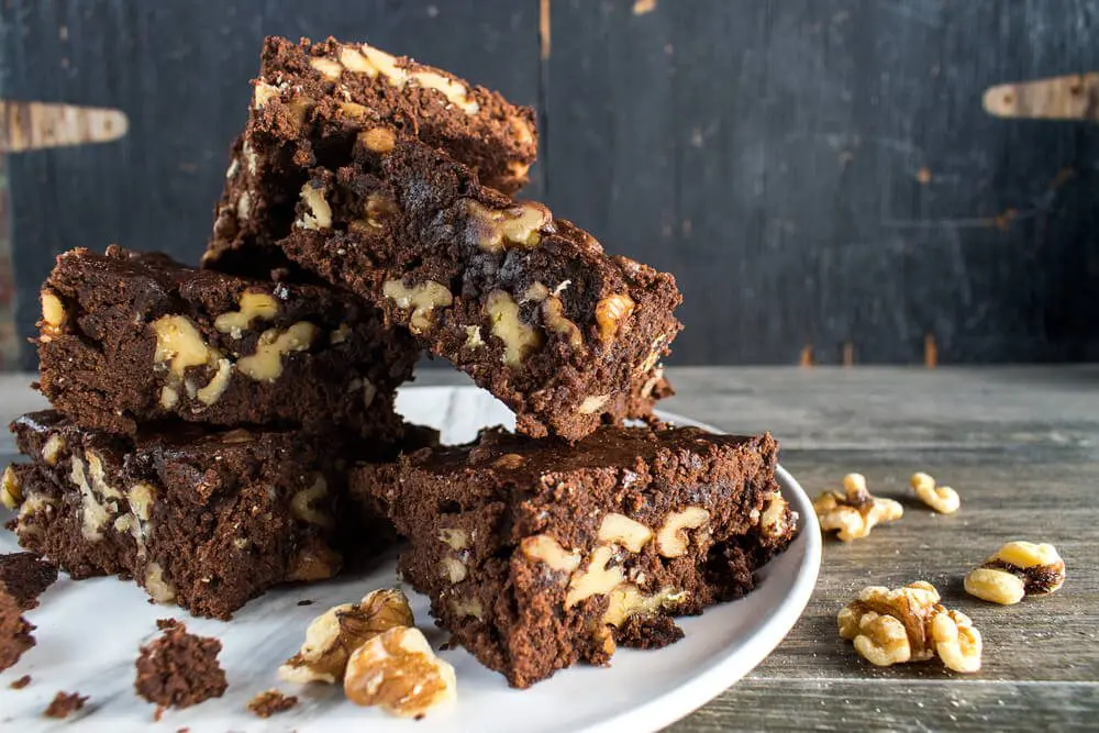 A plate of brownies with walnuts on top.