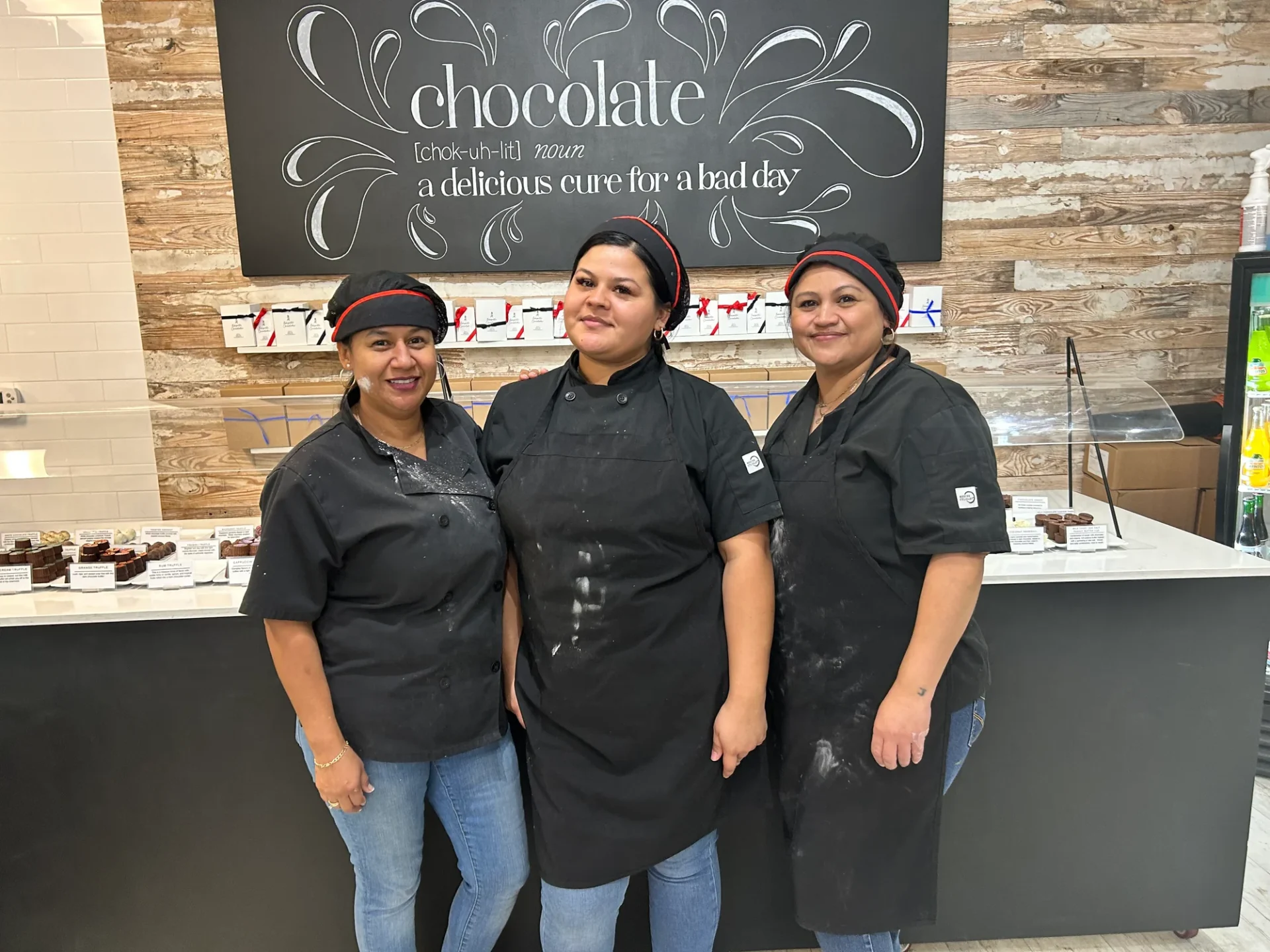 Three women in black aprons standing next to a counter.